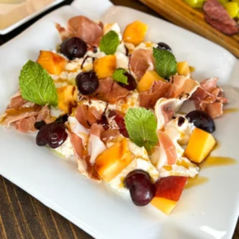 Tommy V's Italian appetizer with prosciutto, melon, cherries, and mint on a white plate.