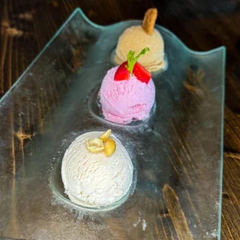 Three scoops of gelato, pink, white, and tan, on a clear glass plate.