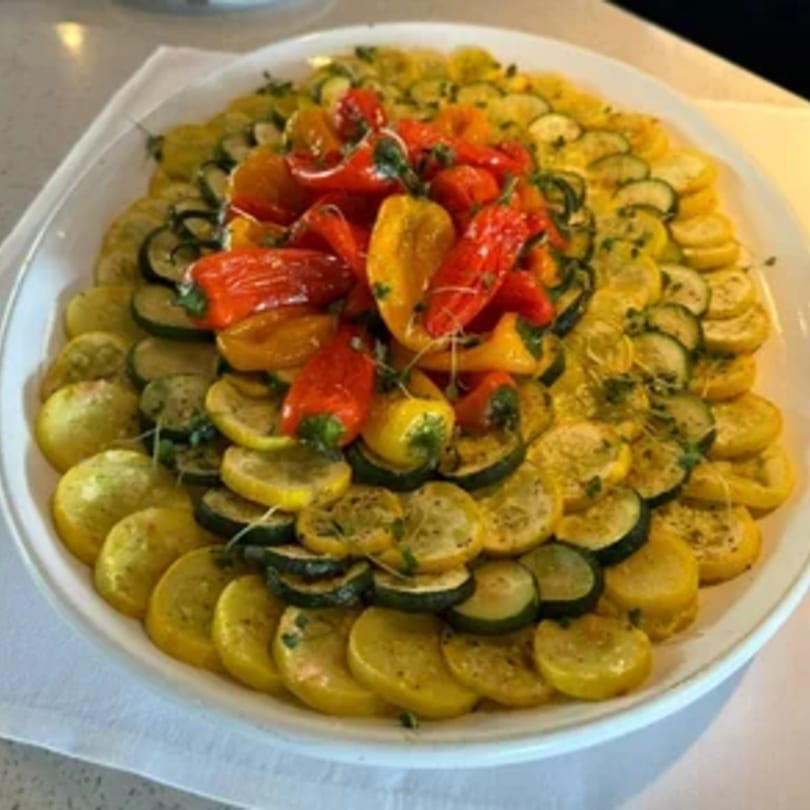 A large platter of roasted zucchini and yellow squash slices, topped with red and yellow bell peppers.