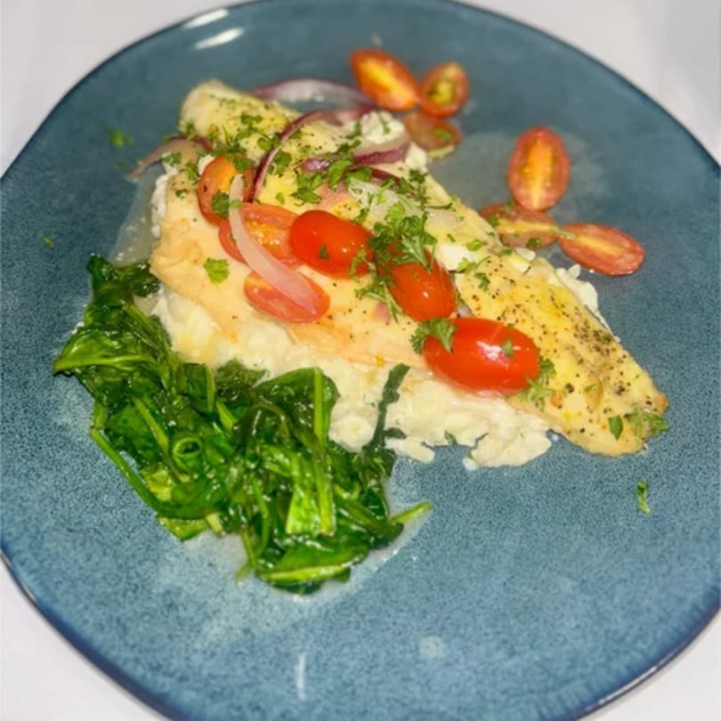 Tommy V's pan-seared fish with cherry tomatoes, red onion, and spinach on a blue plate.