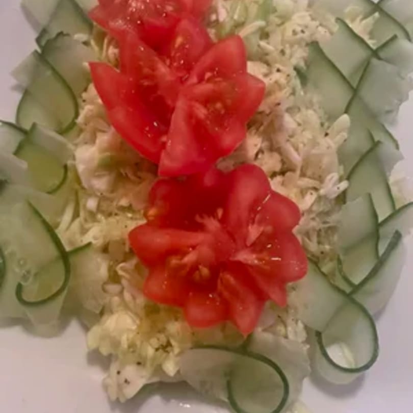 A close-up of a salad with shredded cabbage, cucumber slices, and tomato wedges arranged like flowers.