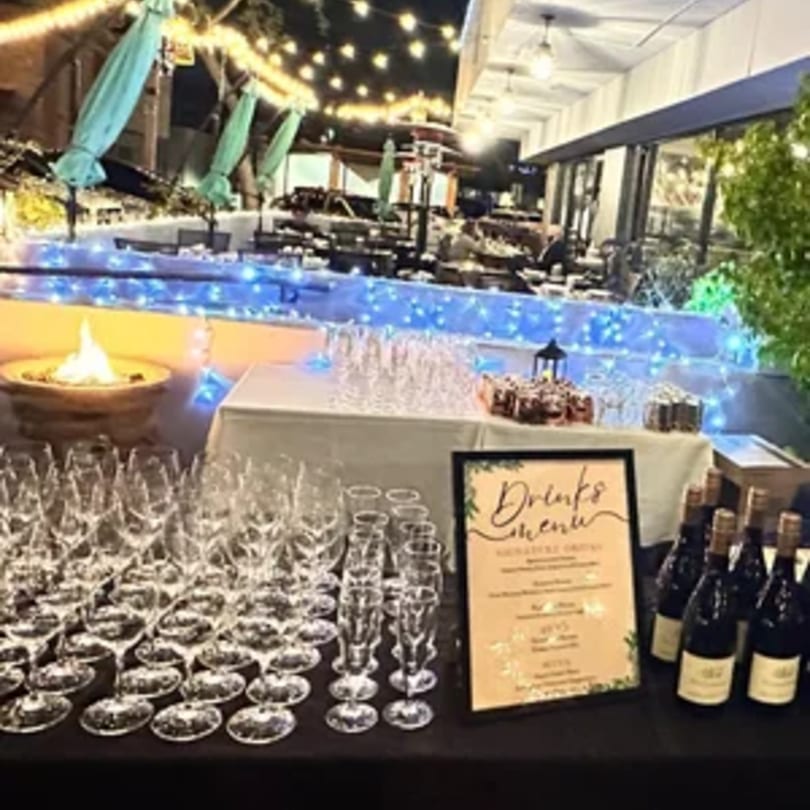 Outdoor bar setup with wine bottles, glasses, a drinks menu, and a fire pit at Tommy V's.