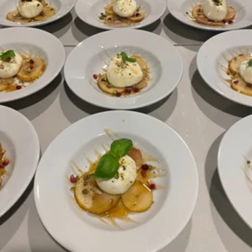 Multiple white plates of Tommy V's Italian burrata appetizer with sliced pears, honey, and basil.