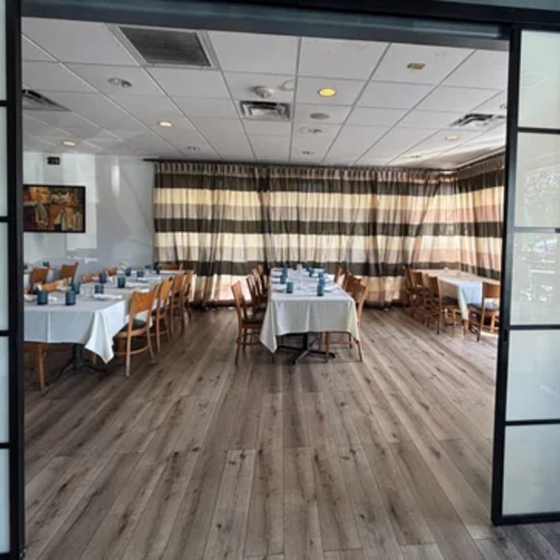 Dining room at Tommy V's Urban Kitchen & Bar with set tables, wooden chairs, and striped curtains.