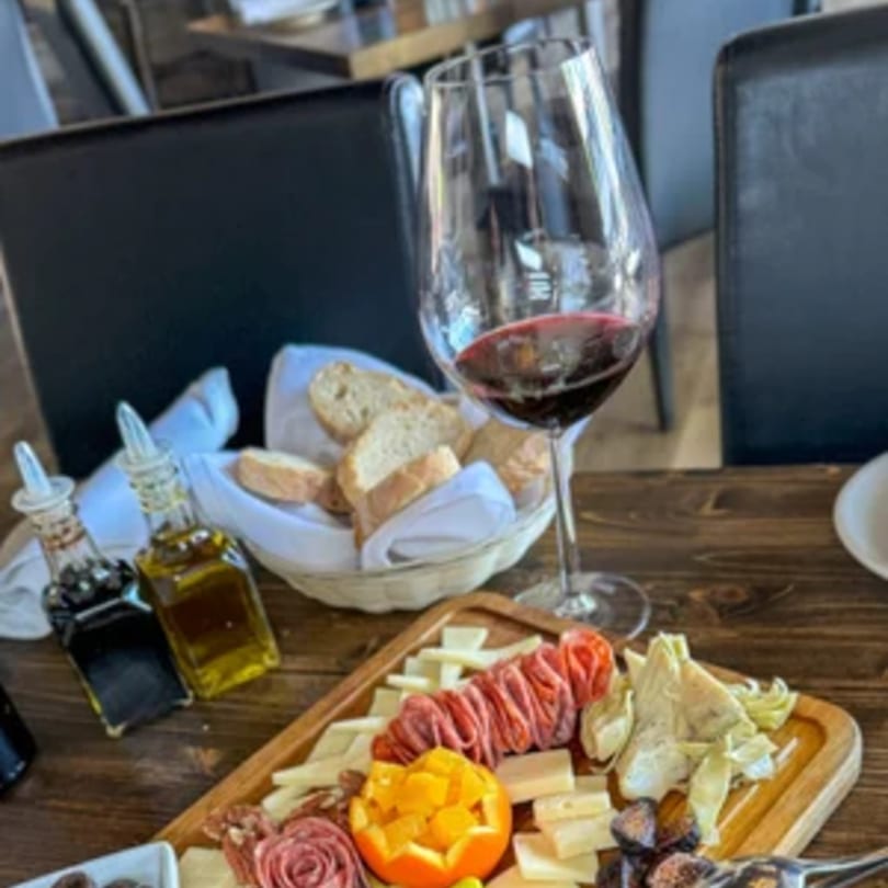 Tommy V's charcuterie board with meats, cheeses, figs, artichokes, bread, and red wine.