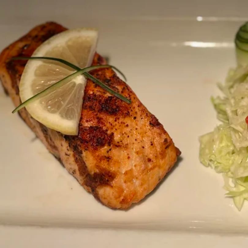 Grilled salmon fillet with a lemon slice and chives, served with a side salad.