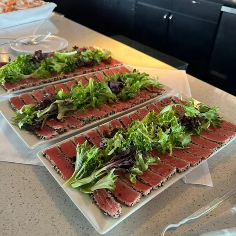 Three long white platters of seared tuna slices topped with fresh green and red lettuce.