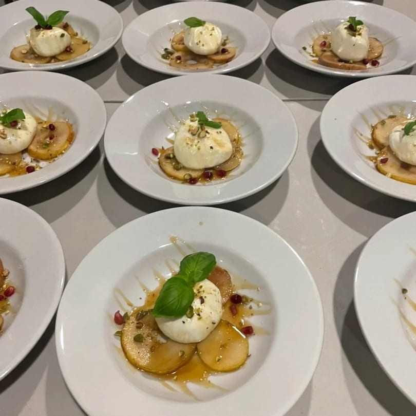 Multiple plates of burrata cheese, sliced pears, basil, pomegranate seeds, and honey drizzle.