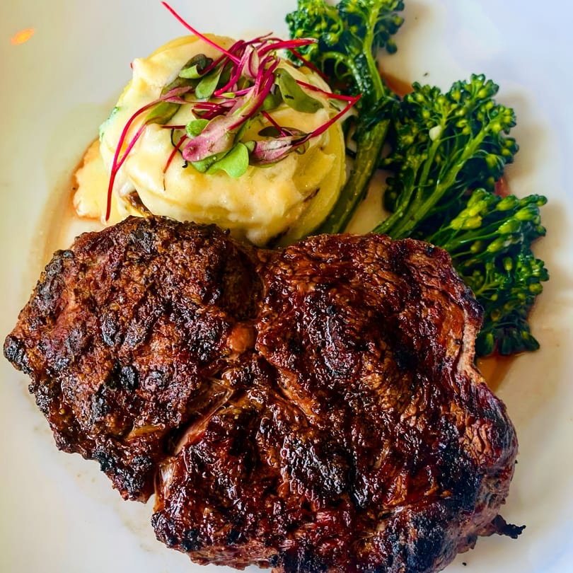 Grilled steak with mashed potatoes topped with microgreens and a side of broccolini.