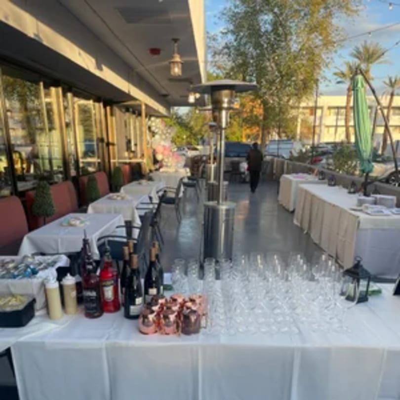 Outdoor patio at Tommy V's with tables set for dining, a bar setup, and a person walking.