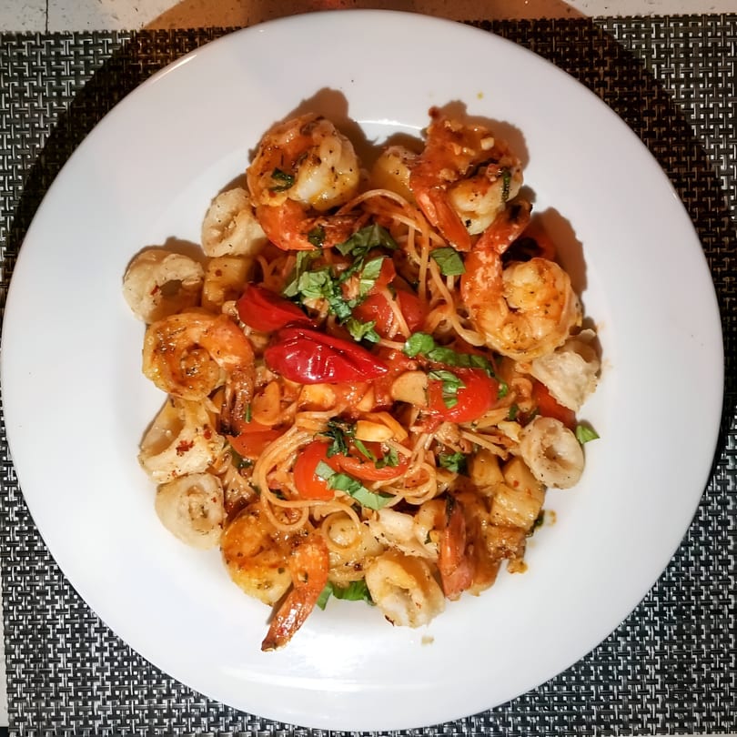 Tommy V's shrimp and calamari pasta with cherry tomatoes and fresh basil on a white plate.