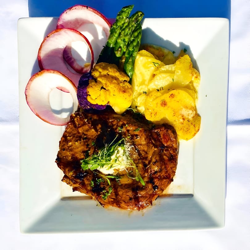Grilled steak with butter, red onions, asparagus, yellow and purple cauliflower, and potatoes.