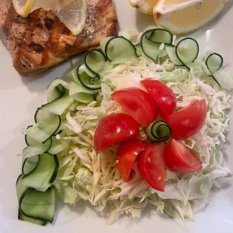 Grilled salmon with lemon slices, a bed of shredded lettuce, cucumber ribbons, and cherry tomatoes.