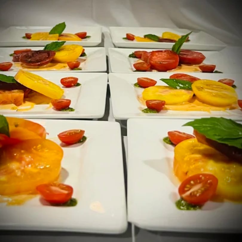 Multiple plates of sliced yellow and red tomatoes with basil and a green sauce.