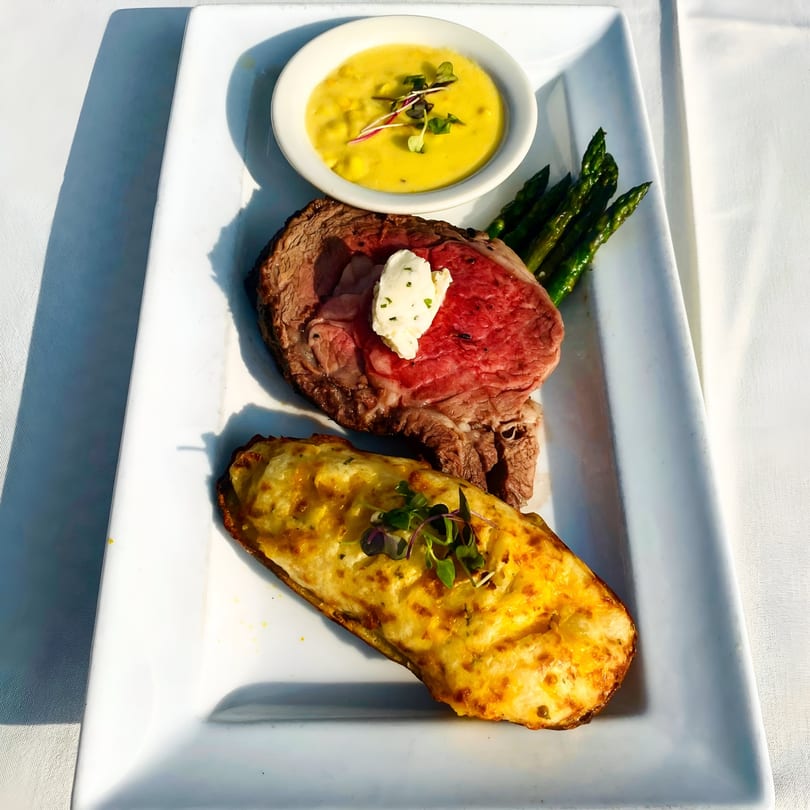 Prime rib with a dollop of butter, asparagus, a twice-baked potato, and a side of corn chowder.